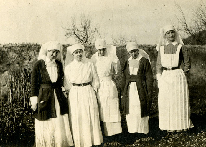 Photographie en noir et blanc de cinq infirmières militaires en uniforme, debout devant un mur.