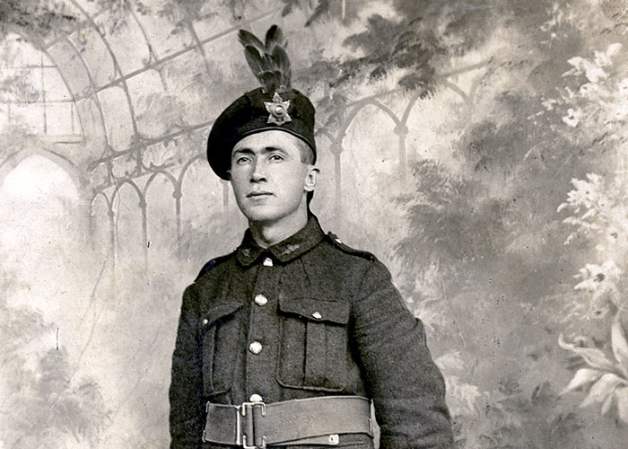 Black and white portrait of a soldier in a military uniform, featuring the Highlanders kilt, stockings, and cap.